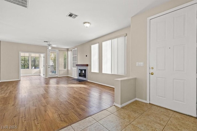 unfurnished living room featuring a fireplace with flush hearth, visible vents, ceiling fan, and wood finished floors