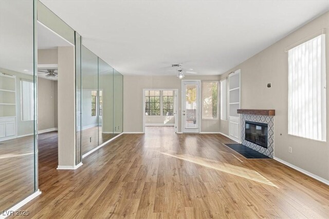 unfurnished living room with hardwood / wood-style floors, built in shelves, a fireplace, and ceiling fan