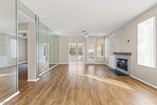 unfurnished living room featuring built in features, a ceiling fan, wood finished floors, a tile fireplace, and baseboards