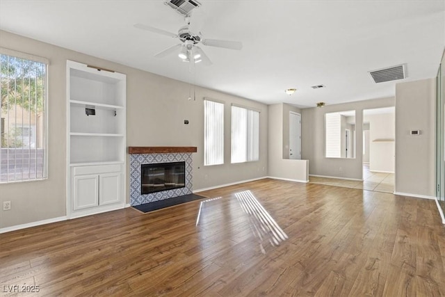 unfurnished living room with plenty of natural light, visible vents, wood finished floors, and a tile fireplace