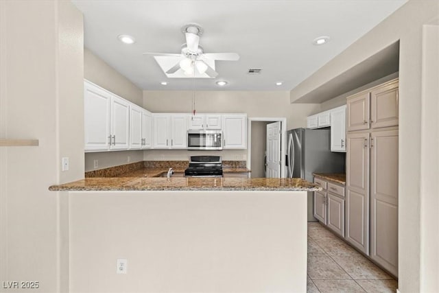 kitchen with light tile patterned floors, kitchen peninsula, stainless steel appliances, light stone countertops, and white cabinets