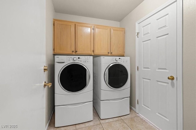 clothes washing area featuring light tile patterned floors, washer and clothes dryer, cabinet space, and baseboards