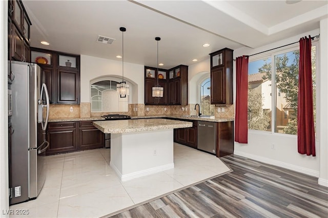 kitchen featuring sink, appliances with stainless steel finishes, light stone counters, a kitchen island, and decorative light fixtures