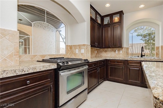 kitchen featuring stainless steel gas range, sink, dark brown cabinets, and backsplash