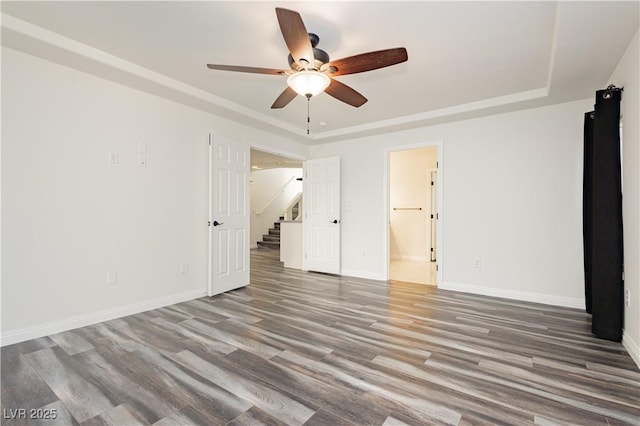 unfurnished bedroom with hardwood / wood-style flooring, ensuite bath, ceiling fan, and a tray ceiling