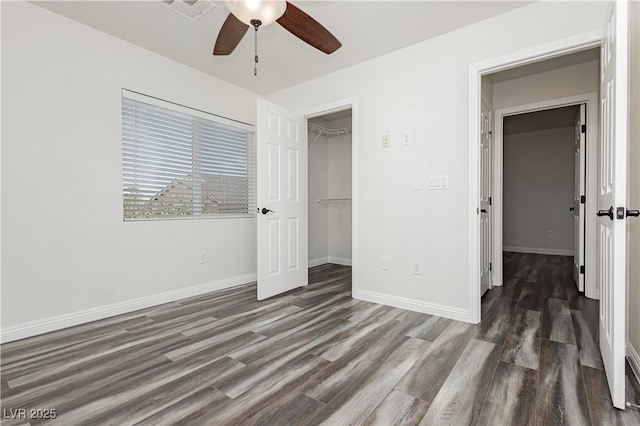 unfurnished bedroom with dark hardwood / wood-style flooring, a spacious closet, a closet, and ceiling fan