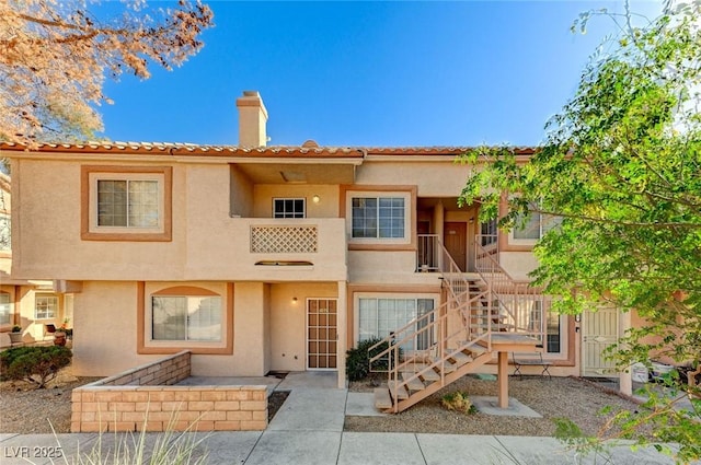 view of front of property featuring a tile roof, stucco siding, a chimney, and stairs