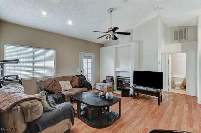 living room featuring a textured ceiling, a fireplace with flush hearth, visible vents, a ceiling fan, and light wood-type flooring