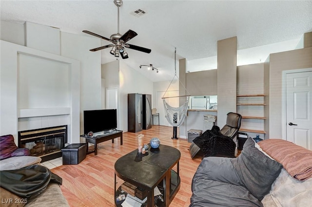 living room featuring light wood finished floors, visible vents, vaulted ceiling, and a tiled fireplace