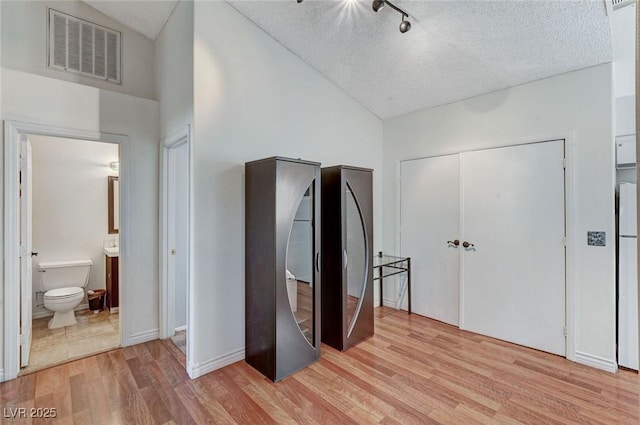 bedroom with visible vents, lofted ceiling, light wood-style flooring, ensuite bathroom, and a textured ceiling