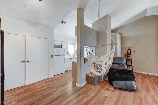 living area with lofted ceiling, visible vents, light wood-style flooring, and a textured ceiling