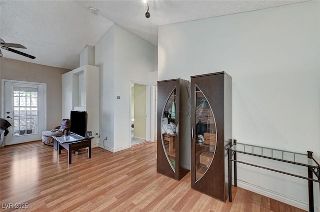 interior space with light wood finished floors, a ceiling fan, a textured ceiling, high vaulted ceiling, and baseboards