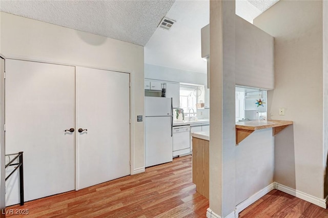 kitchen featuring white appliances, visible vents, light wood-style flooring, a peninsula, and light countertops