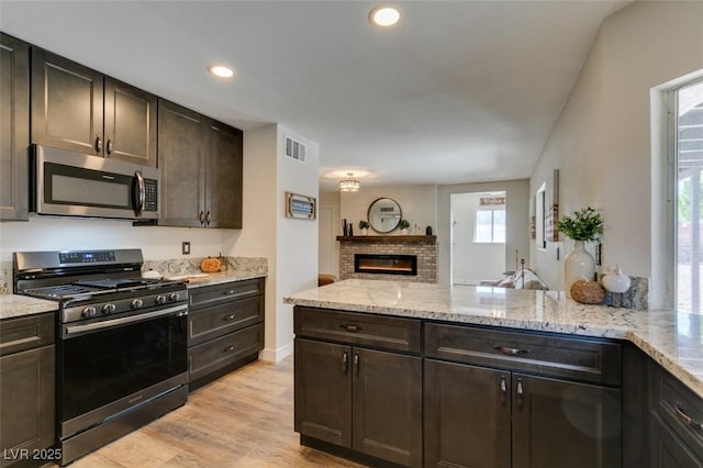 kitchen featuring dark brown cabinetry, appliances with stainless steel finishes, kitchen peninsula, light stone countertops, and light hardwood / wood-style floors