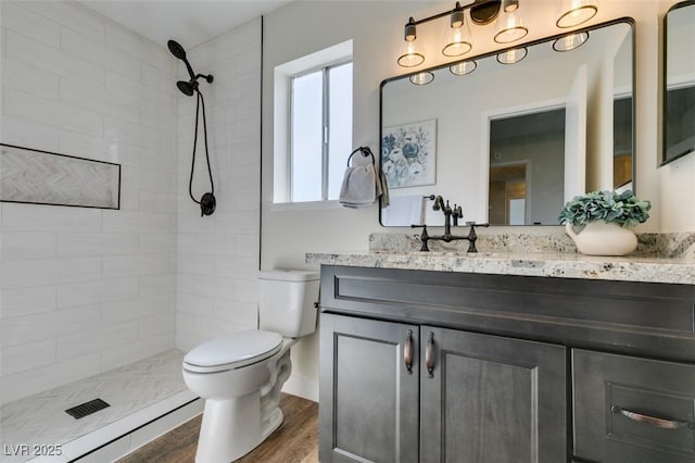 bathroom with vanity, a tile shower, hardwood / wood-style floors, and toilet