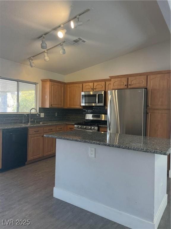 kitchen featuring vaulted ceiling, appliances with stainless steel finishes, tasteful backsplash, dark stone counters, and dark wood-type flooring