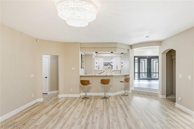 kitchen with french doors, a breakfast bar, an inviting chandelier, kitchen peninsula, and light hardwood / wood-style floors