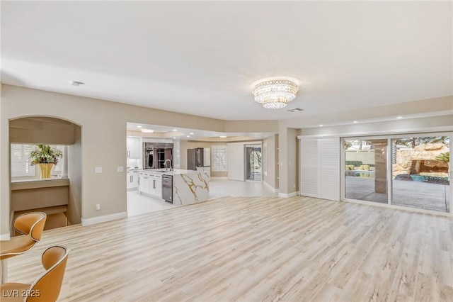 unfurnished living room with sink, a wealth of natural light, an inviting chandelier, and light hardwood / wood-style flooring