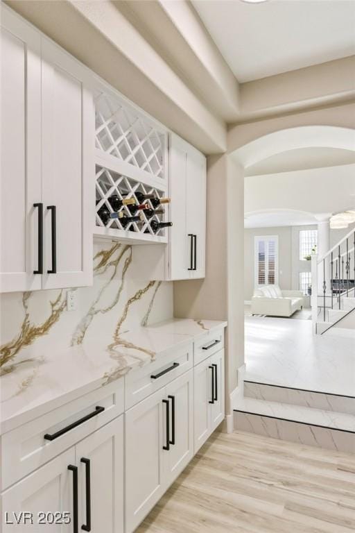 bar featuring backsplash, light stone countertops, light hardwood / wood-style flooring, and white cabinets