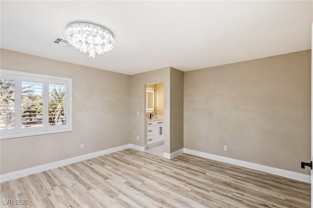 spare room featuring a notable chandelier and light wood-type flooring