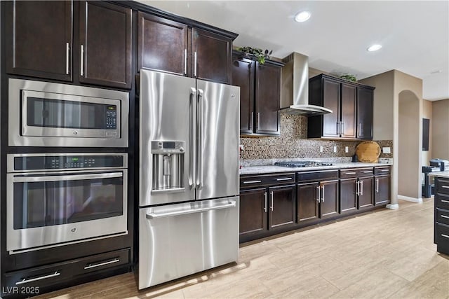 kitchen with tasteful backsplash, stainless steel appliances, dark brown cabinets, and wall chimney range hood