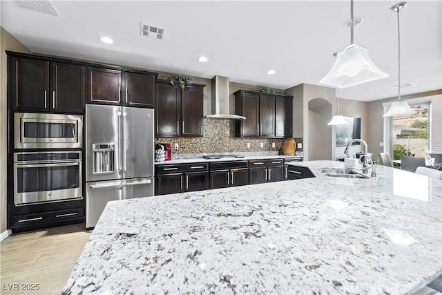 kitchen featuring sink, appliances with stainless steel finishes, hanging light fixtures, tasteful backsplash, and wall chimney exhaust hood