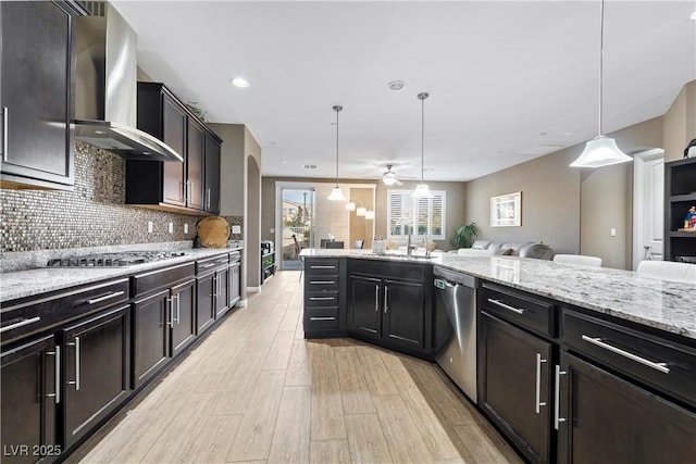 kitchen with backsplash, appliances with stainless steel finishes, decorative light fixtures, and wall chimney range hood