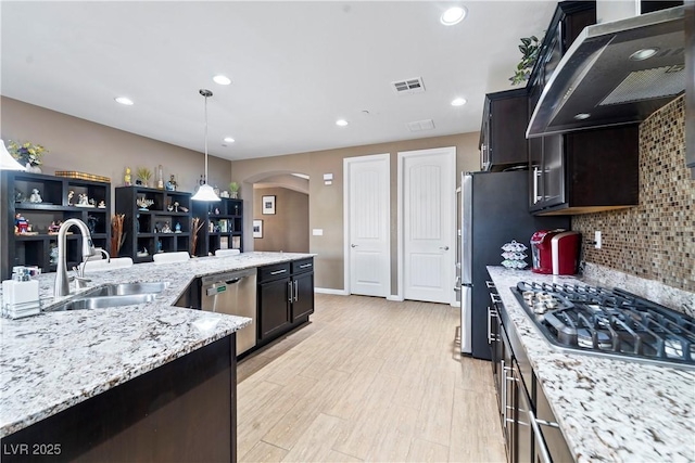 kitchen featuring wall chimney exhaust hood, sink, pendant lighting, stainless steel appliances, and light stone countertops