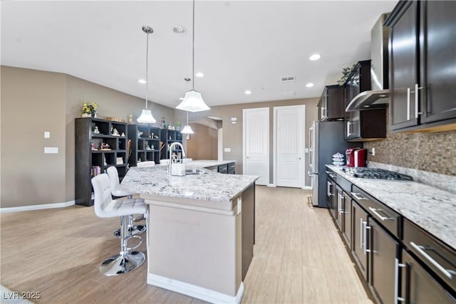 kitchen with pendant lighting, sink, a center island with sink, light stone countertops, and a kitchen bar