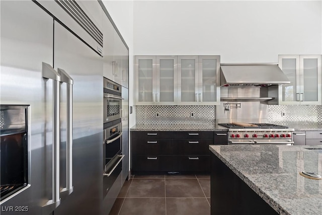 kitchen featuring light stone counters, extractor fan, tasteful backsplash, dark tile patterned flooring, and stainless steel built in fridge