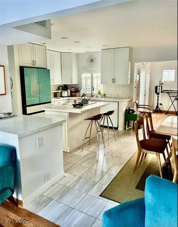 kitchen featuring light tile patterned floors, a breakfast bar area, backsplash, fridge, and white dishwasher