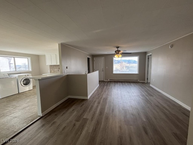 unfurnished living room featuring sink, dark hardwood / wood-style floors, ceiling fan, washing machine and dryer, and a baseboard heating unit