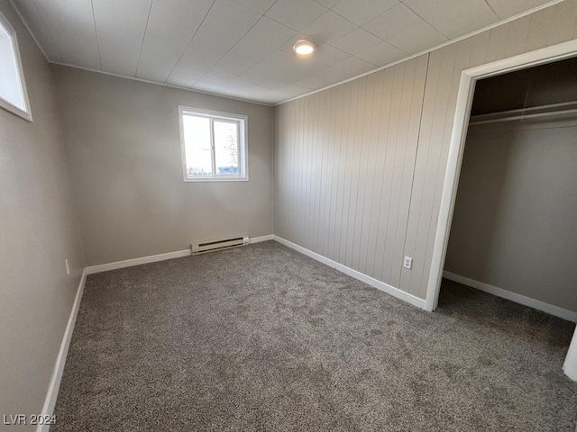 unfurnished bedroom with carpet, wooden walls, baseboard heating, and a closet