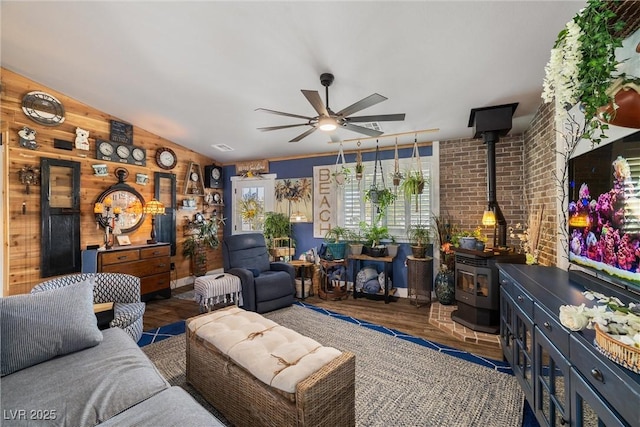 living room featuring wood walls, dark hardwood / wood-style floors, ceiling fan, and a wood stove