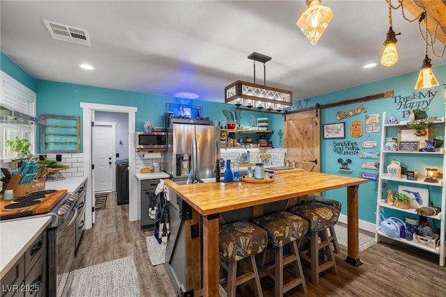 kitchen with butcher block counters, hanging light fixtures, stainless steel appliances, decorative backsplash, and a barn door