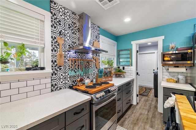 kitchen featuring tasteful backsplash, stainless steel appliances, light wood-type flooring, and wall chimney range hood