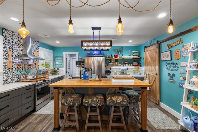 kitchen with hardwood / wood-style flooring, backsplash, stainless steel appliances, a barn door, and wall chimney exhaust hood