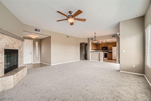 unfurnished living room featuring a tiled fireplace, a wealth of natural light, light colored carpet, and ceiling fan