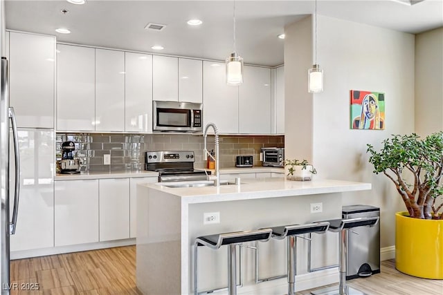 kitchen featuring light hardwood / wood-style flooring, hanging light fixtures, stainless steel appliances, tasteful backsplash, and white cabinets