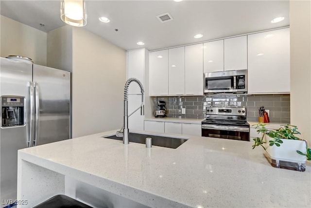 kitchen with sink, appliances with stainless steel finishes, white cabinetry, hanging light fixtures, and decorative backsplash