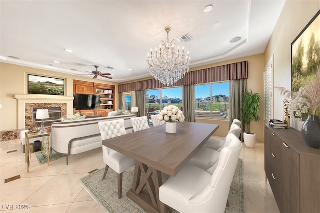 tiled dining room with a fireplace and ceiling fan with notable chandelier