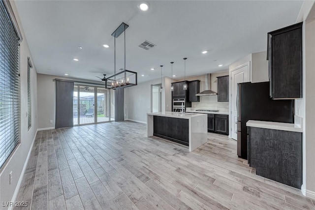 kitchen featuring pendant lighting, an island with sink, wall chimney exhaust hood, and appliances with stainless steel finishes