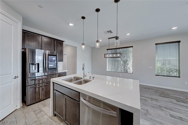 kitchen with sink, a center island with sink, pendant lighting, stainless steel appliances, and light hardwood / wood-style floors