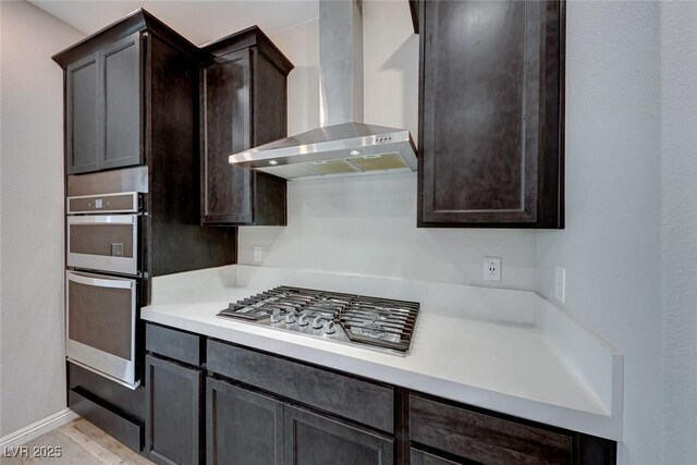 kitchen featuring dark brown cabinetry, wall chimney range hood, light tile patterned floors, and stainless steel appliances