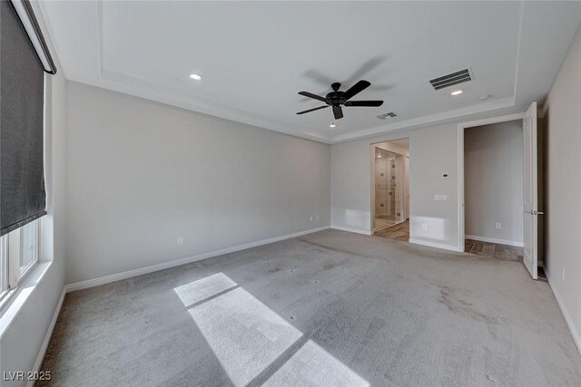 unfurnished bedroom featuring ceiling fan, ensuite bathroom, a raised ceiling, and light colored carpet