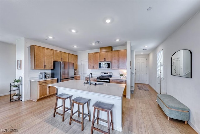 kitchen featuring sink, a kitchen island with sink, stainless steel appliances, a kitchen breakfast bar, and light hardwood / wood-style floors