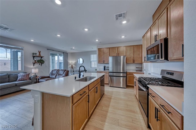 kitchen featuring sink, light hardwood / wood-style flooring, a breakfast bar area, appliances with stainless steel finishes, and a center island with sink