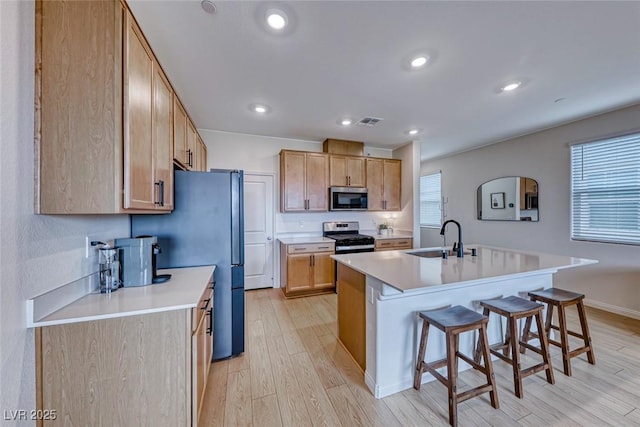 kitchen featuring sink, light wood-type flooring, appliances with stainless steel finishes, a kitchen breakfast bar, and an island with sink