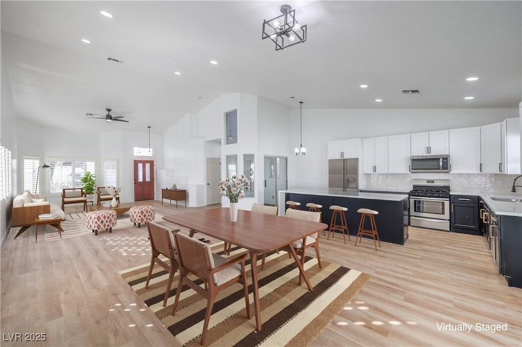 dining area with sink, ceiling fan with notable chandelier, high vaulted ceiling, and light wood-type flooring