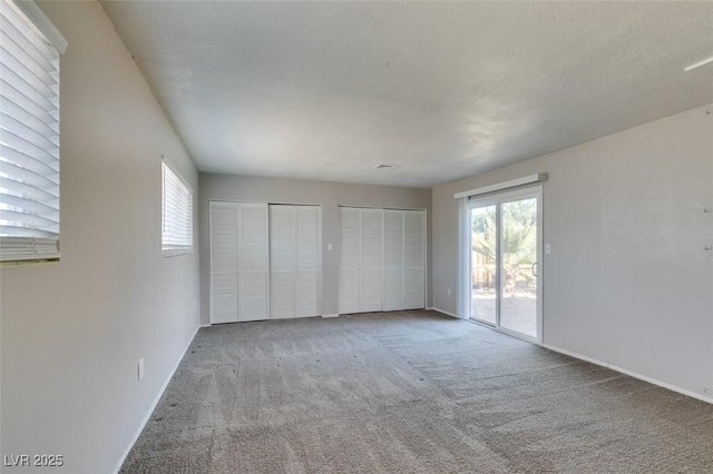 unfurnished bedroom with a textured ceiling, access to outside, multiple closets, and carpet